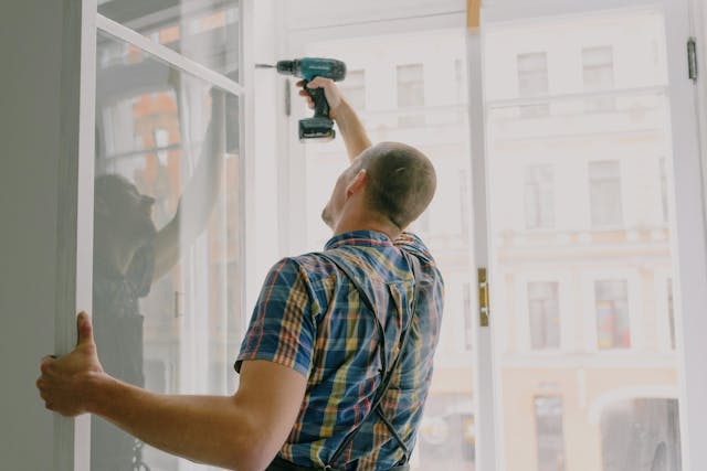 man drilling into open window frame